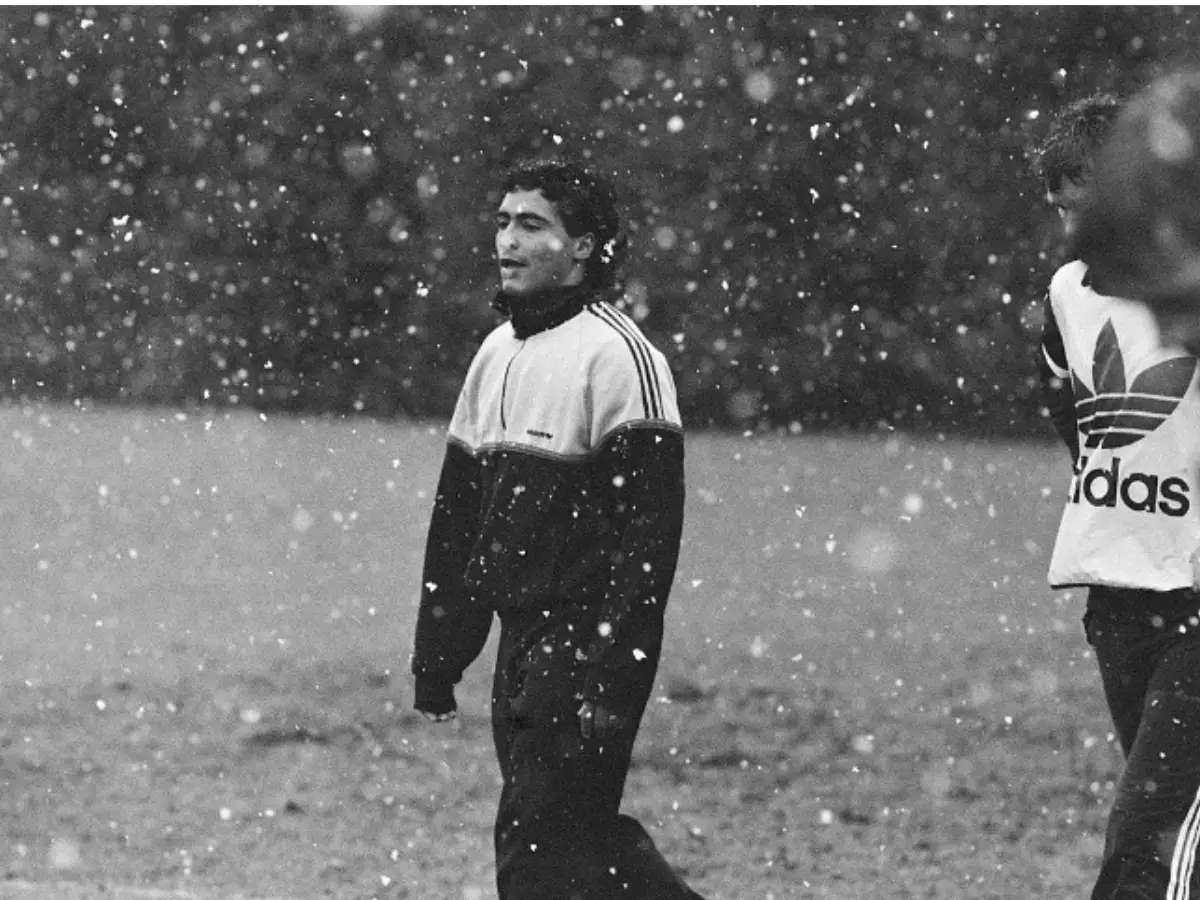 O atacante Romário sorri em sobre um gramado enquanto chove, utilizando um conjunto esportivo durante um treinamento
