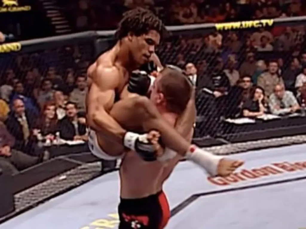 Fotografia do momento em que Matt Hughes ergue Carlos Newton no UFC 34, preparando o golpe que resultou em um nocaute bizarro