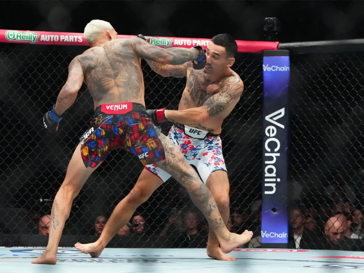 Max Holloway, de luvas vermelhas, e Charles Oliveira, de luvas azuis, em uma troca de golpes franca durante o UFC 326 na T-Mobile Arena.