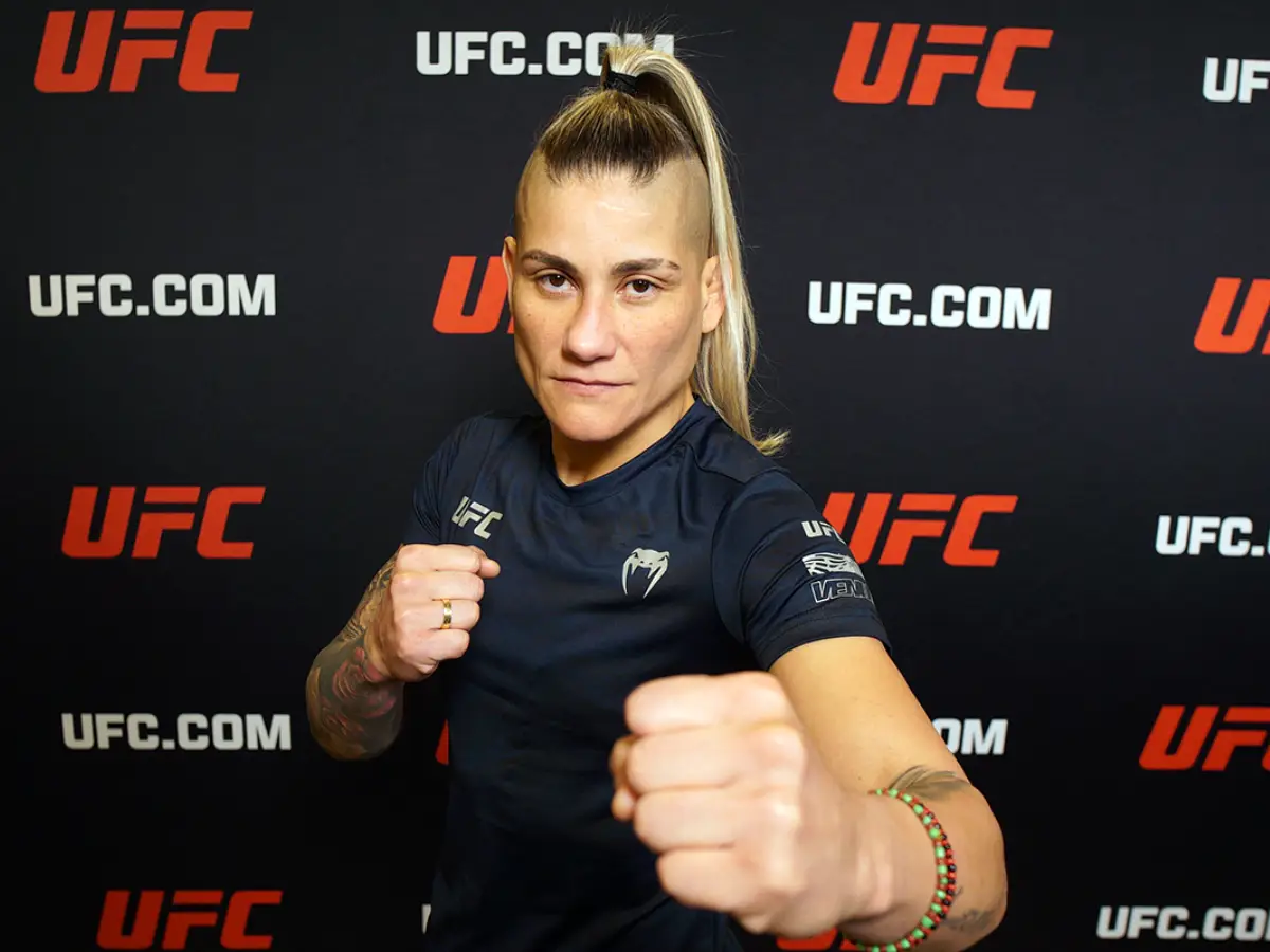 A peso-mosca brasileira Priscila "Pedrita" Cachoeira posa para foto oficial com o uniforme do UFC; a atleta exibe seu característico penteado moicano loiro e as laterais do cabelo raspadas, simbolizando sua prontidão para o duelo contra Alice Pereira.